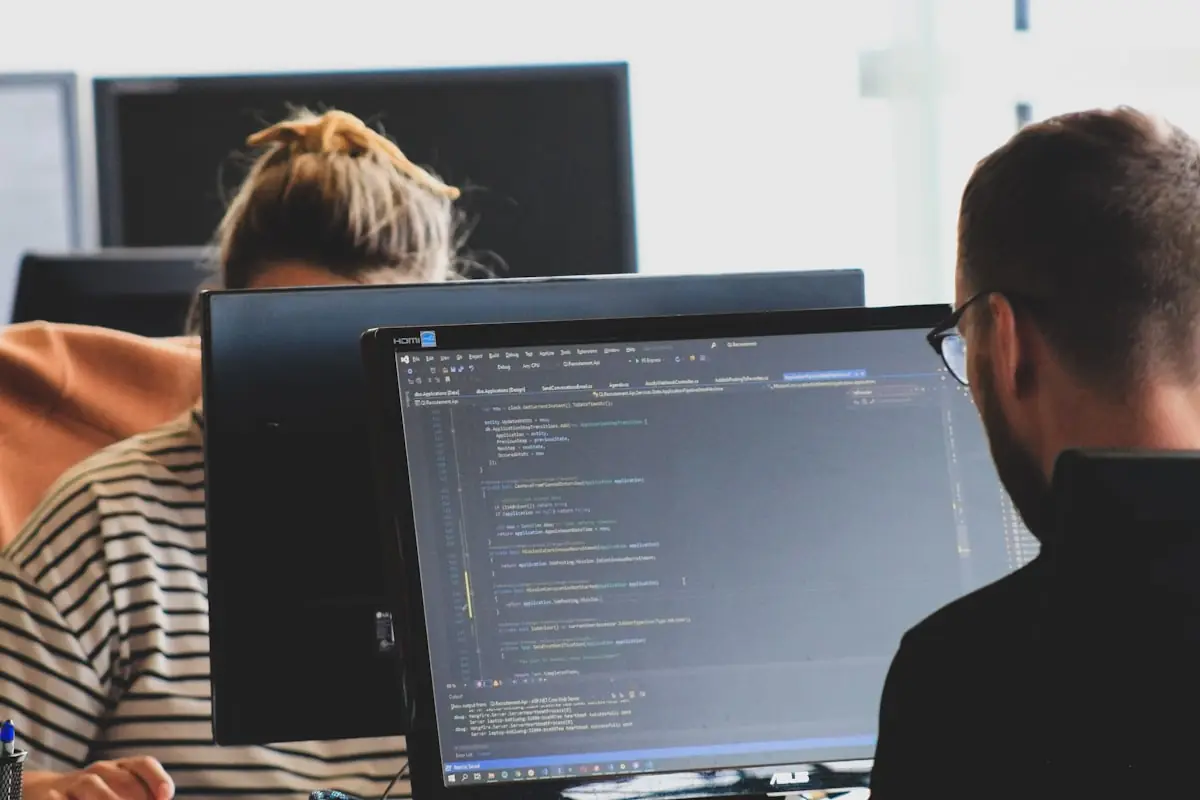 Two engineers reviewing code together at adjacent monitors